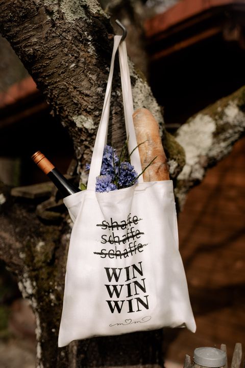 Eine Tragetasche mit Text, die an einem Baumzweig hängt und ein Baguette und Blumen enthält.
