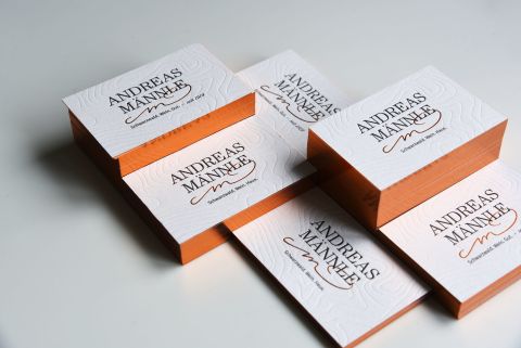Mehrere verschieden hohe Stapel weißer Visitenkarten mit kupferfarbenem Rand und der Aufschrift "Andreas Männle" in schwarz, von oben fotografiert.