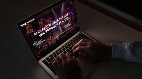 Nahaufnahme eines Laptops mit einer Website zur Event-Produktion, die eine Show mit Lichteffekten und Publikum zeigt.