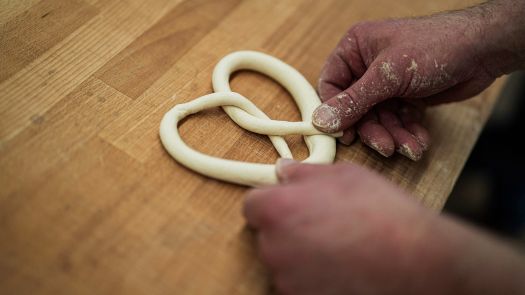 Hände formen frischen Brezelteig auf einem Holztisch in traditioneller Backstube.