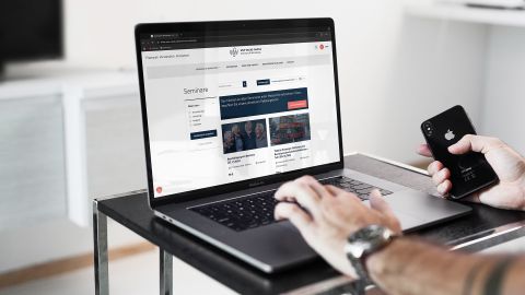Person durchsucht die WSW-Campus Website nach Seminaren auf Laptop, Smartphone in der Hand