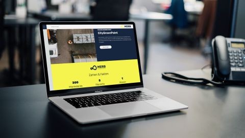 Laptop zeigt MERB-Webseite mit Informationen zu Mitarbeitenden, Standorten und Mission im modernen Büro.