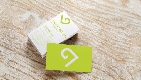 Visitenkartenstapel von Back to Activity auf hellem Holztisch, Vorderseite mit grünem Logo.
