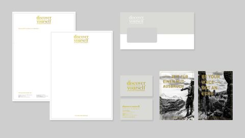Geschäftsausstattung von „discover yourself“ mit Briefpapier, Visitenkarten, Umschlag und Motivpostern auf grauem Hintergrund.