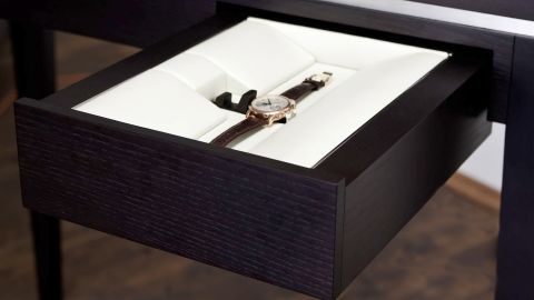 Offene Schublade mit edler Armbanduhr auf weißer Polsterung in dunklem Holzgehäuse zur stilvollen Aufbewahrung.