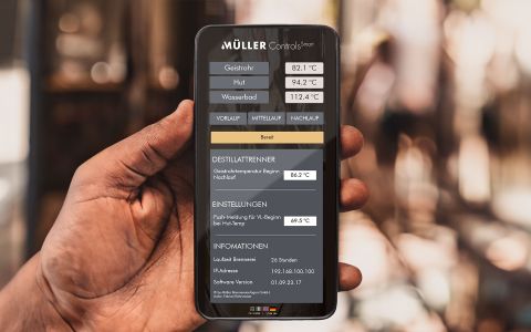 Müller Controls Smart App zur Destillationssteuerung Hand hält ein Smartphone mit der Müller Controls Smart App zur digitalen Steuerung einer Destillationsanlage, angezeigt sind Temperaturwerte und Einstellungen.