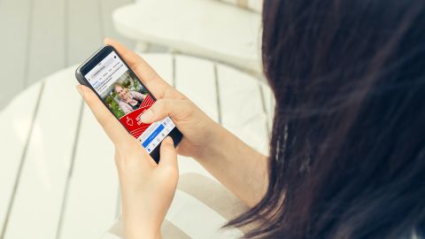 Eine Frau hält ein Smartphone mit geöffneter Facebook-Seite von Ernteretter Ortenau mit Bild und rotem Infopost.