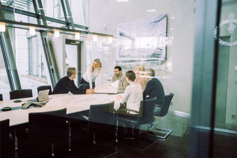 Teammeeting in modernem Büro mit Glaswänden, großen Fenstern und Architekturmodellen auf dem Tisch.