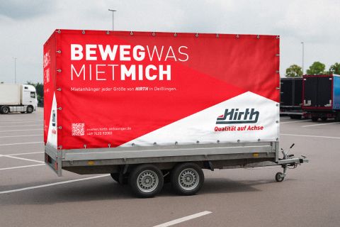 Doppelachser Pkw-Anhänger Hirth Anhänger mit rot-weißer Plane auf einem Parkplatz.