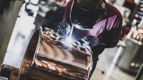 Schweißarbeiten an einem Kupferbauteil für eine Destillationsanlage Schweißer mit Schutzhelm und Handschuhen bearbeitet präzise ein glänzendes Kupferbauteil für eine Destillationsanlage.