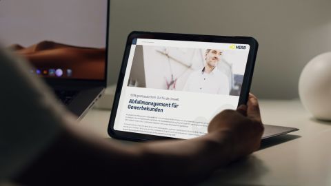 Tablet zeigt MERB-Webseite mit Informationen zum Abfallmanagement für Gewerbekunden, im Hintergrund ein Laptop.