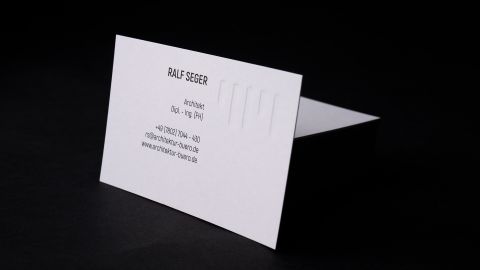 Elegante, weiße Visitenkarte von Architekturbüro Müller + Partner mit Prägung, aufgestellt vor schwarzem Hintergrund.