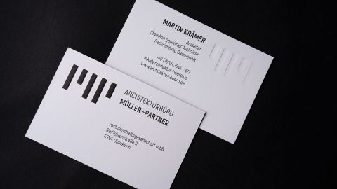 wei weiße Visitenkarten von Architekturbüro Müller + Partner mit Prägung und modernem Design auf schwarzem Hintergrund.