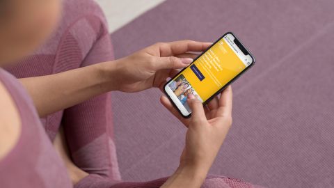 Person in Sportkleidung hält ein Smartphone mit einer gelben Website mit Text.