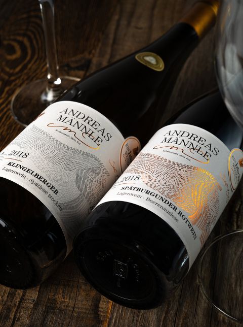 Zwei Flaschen Wein liegen dicht beieinander auf einem dunklen Holztisch.