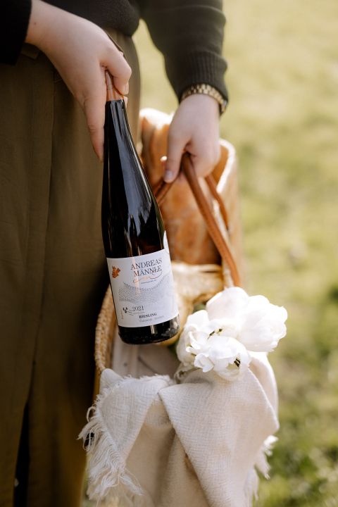 A woman holding a wine bottle in a basket, perfect for a picnic or celebration.