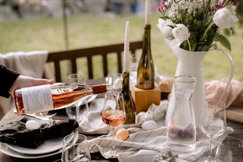 Eleganter Tisch mit Roséwein, Blumenarrangement, Kerzen und Geschirr für ein stilvolles Outdoor-Dinner.