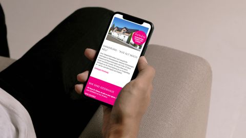 Person hält Smartphone mit geöffneter Ideenhaus-Webseite zur Sanierung unter dem Motto „Aus alt mach neu“.