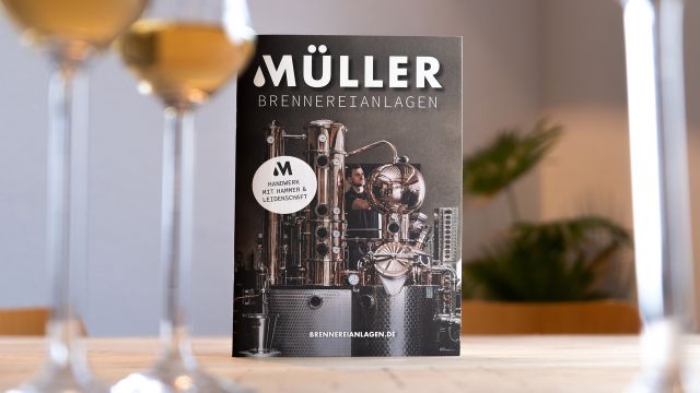 Werbebroschüre von Müller Brennereianlagen mit glänzender Destillationsanlage, aufgestellt auf einem Tisch mit Schnapsgläsern im Vordergrund.
