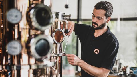 Wartung einer Kupfer-Destillationsanlage Ein Techniker in schwarzem Poloshirt justiert mit einem Schraubenzieher eine Kupfer-Destillationsanlage in einer Werkstatt.