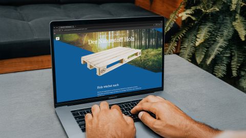 Laptop mit geöffneter Website über Holzpaletten und nachhaltigen Rohstoff Holz.