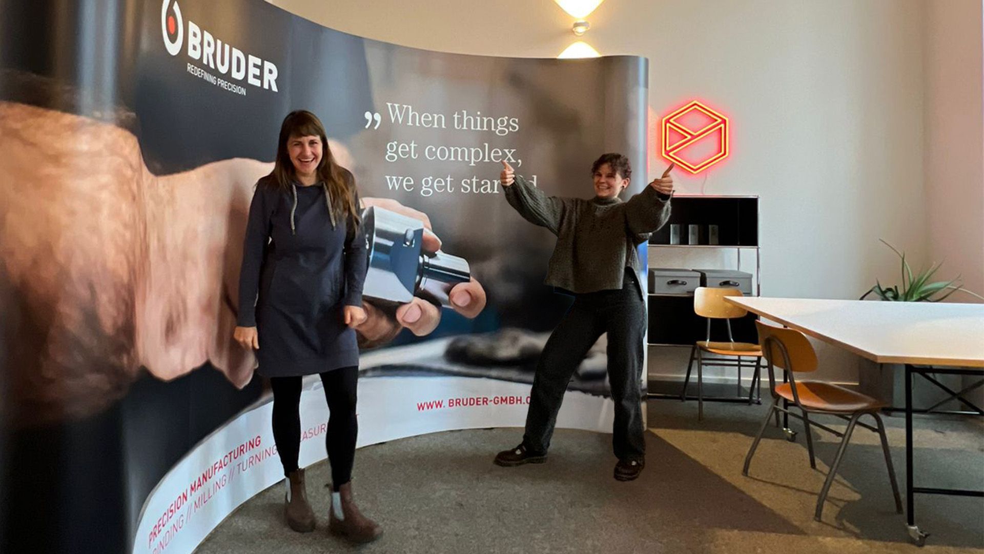 Zwei Personen vor einem Bruder-Werbestand mit dem Slogan „When things get complex, we get started“ in modernem Büroambiente.