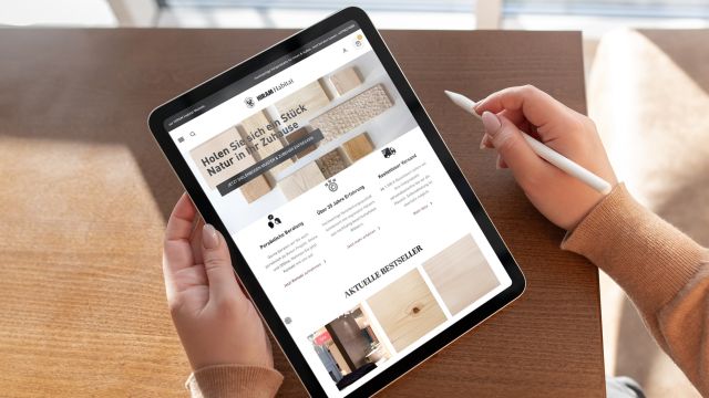 Person hält Tablet mit HIRAM Habitat-Shop, der nachhaltige Holzprodukte und Bestseller zeigt