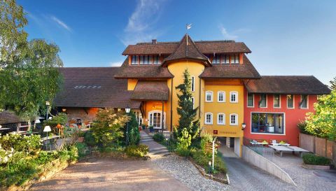 Landhotel Krone Außenansicht im Sommer Hotelgebäude Krone mit gelb-roter Fassade, traditionellem Dach und grüner Gartenanlage bei strahlendem Sonnenschein.
