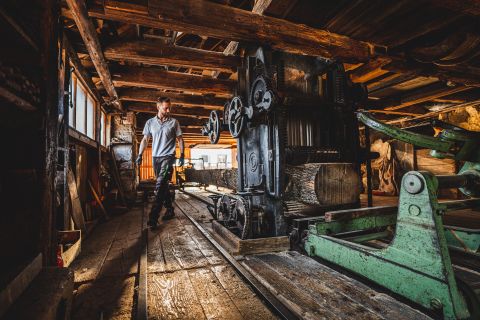 Mann in traditioneller Werkstatt mit altem Sägewerk und Baumstamm in rustikaler Umgebung aus Holz