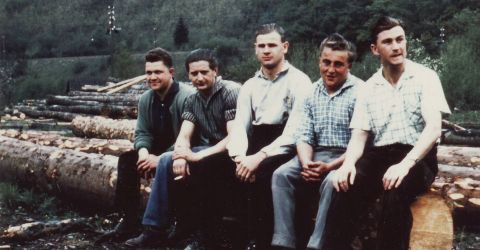 Historische Aufnahme von Waldarbeitern Fünf Männer in Arbeitskleidung sitzen auf Baumstämmen im Wald, historische Aufnahme aus der Holzverarbeitung.