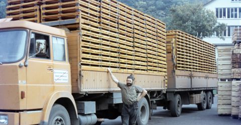Historische Aufnahme von LKW mit Palettenlieferung Fahrer steht lächelnd vor beladenem LKW mit gestapelten Holzpaletten auf dem Werksgelände, historische Aufnahme aus dem 20. Jahrhundert.