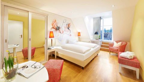 Gemütliches Hotelzimmer mit Doppelbett, floraler Wandgestaltung, roten Akzenten und Zugang zu einem kleinen Balkon.