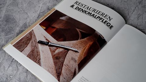 Aufgeschlagene Broschüre von Jogerst Steintechnologie zum Thema Restaurieren und Denkmalpflege mit großformatigem Bild euner Sandsteinstruktur mit Meißel.
