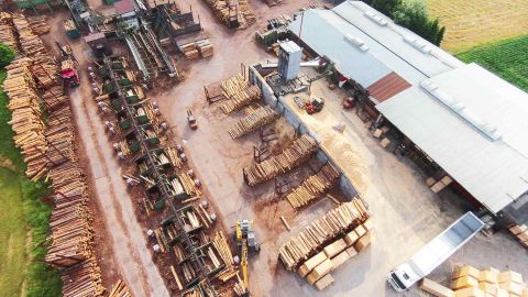 Luftaufnahme eines modernen Sägewerks mit gestapelten Holzstämmen, Förderanlagen und Produktionshallen.