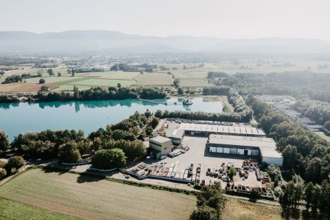 Luftaufnahme einer Abfall-Sortieranlage neben einem türkisblauen See, umgeben von Feldern und Wald.