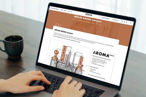 Website von Müller Brennereianlagen auf Laptop Person nutzt einen Laptop und betrachtet die Website von Müller Brennereianlagen mit Informationen zur AROMA Compact Destillationsanlage.