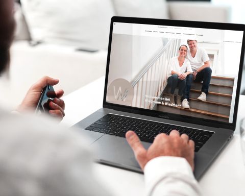 Ein Mann in weißem Hemd nutzt einen Laptop, auf dem die Website von Wiedmann & Wiedmann mit einem Begrüßungsbild geöffnet ist.