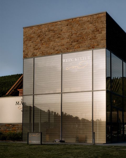 Weingutgebäude mit Glas- und Steinfassade, reflektierend im Abendlicht.