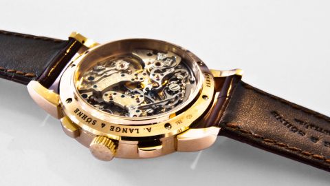 Luxuriöse A. Lange & Söhne Uhr mit goldener Rückseite und sichtbarem Uhrwerk auf braunem Lederarmband.