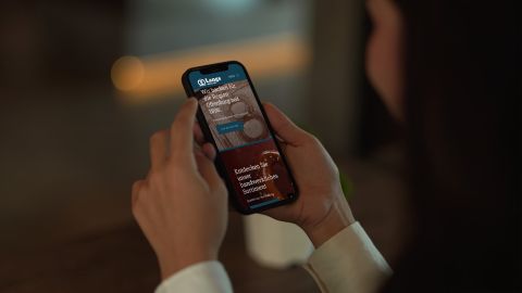 Eine Person hält ein Smartphone und surft auf der Website von Langs Backstube, die handwerkliches Backwarensortiment präsentiert.