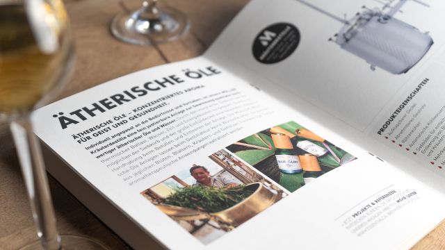 Aufgeschlagene Broschüre von Müller Brennereianlagen mit Informationen zur Destillation ätherischer Öle und Produktbildern.